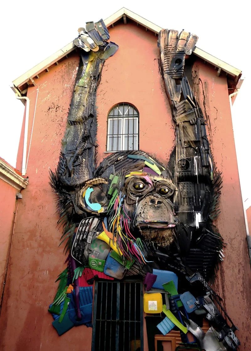 Macaco gigante em relevo pendurado na fachada rosa de uma casa, feito de resíduos