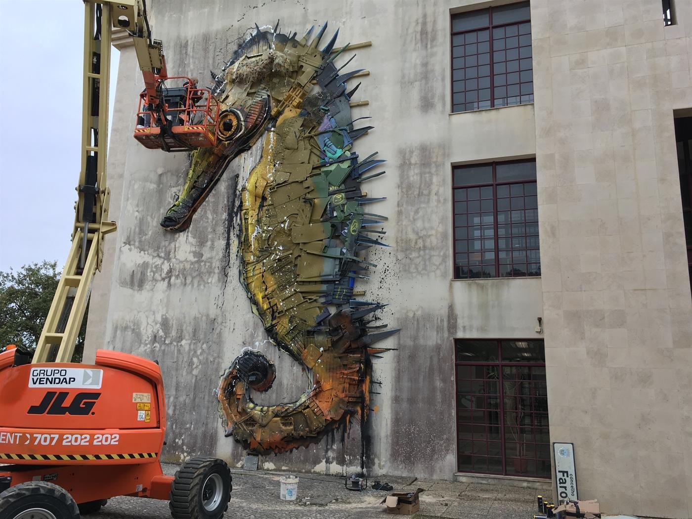 Cavalo-marinho gigante a ser montado numa parede, com uma plataforma elevatória laranja
