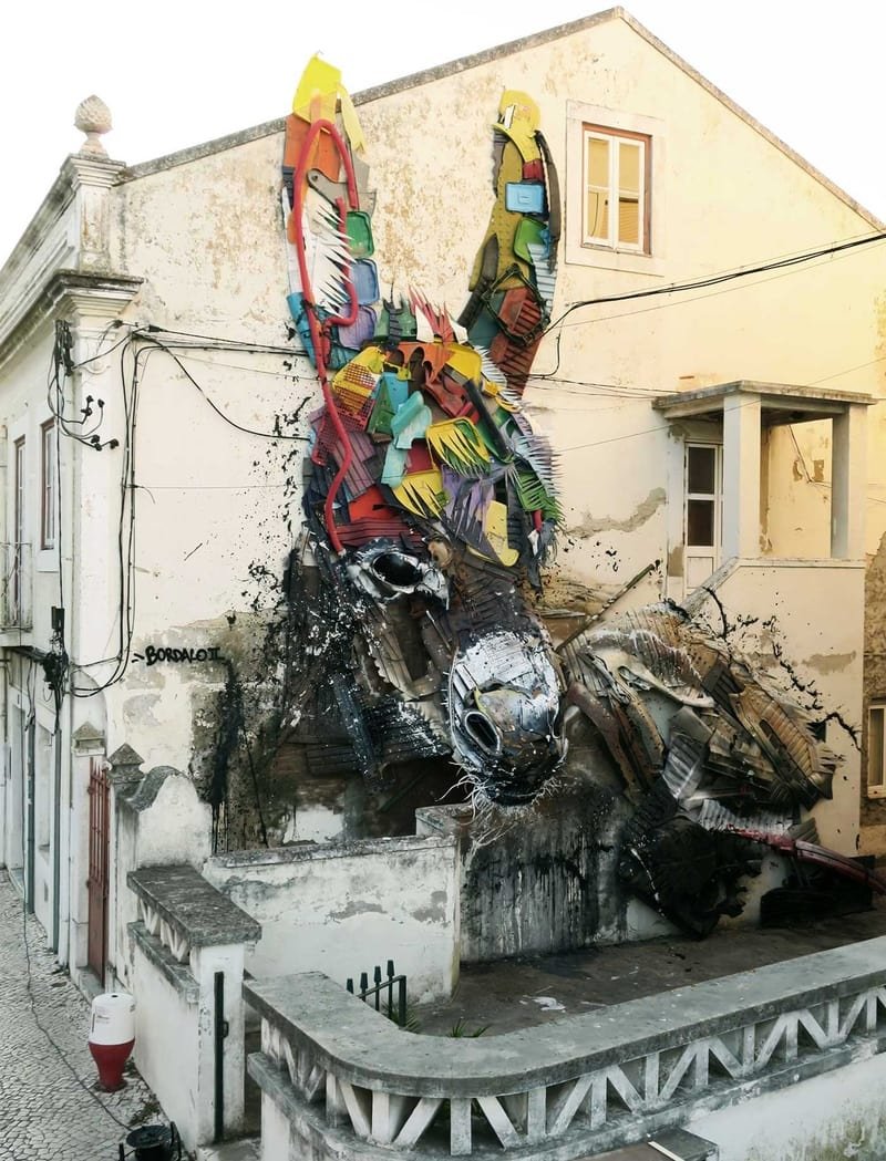 Burro em relevo numa fachada branca degradada, com orelhas de plástico colorido