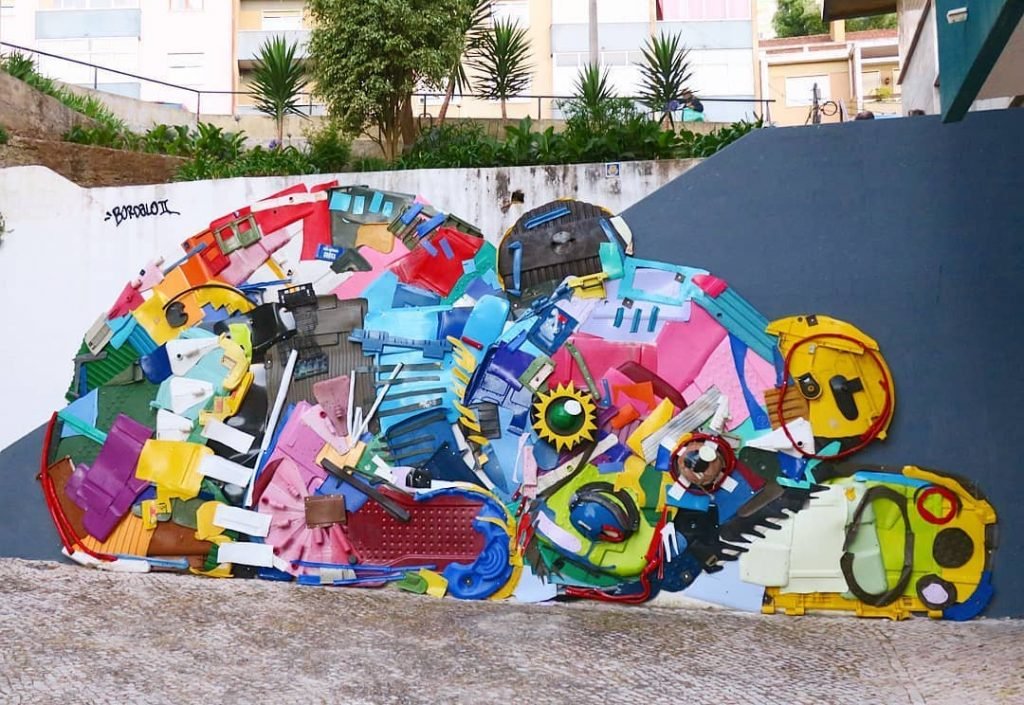 Animal deitado feito de plásticos muito coloridos, em relevo ao longo de um muro