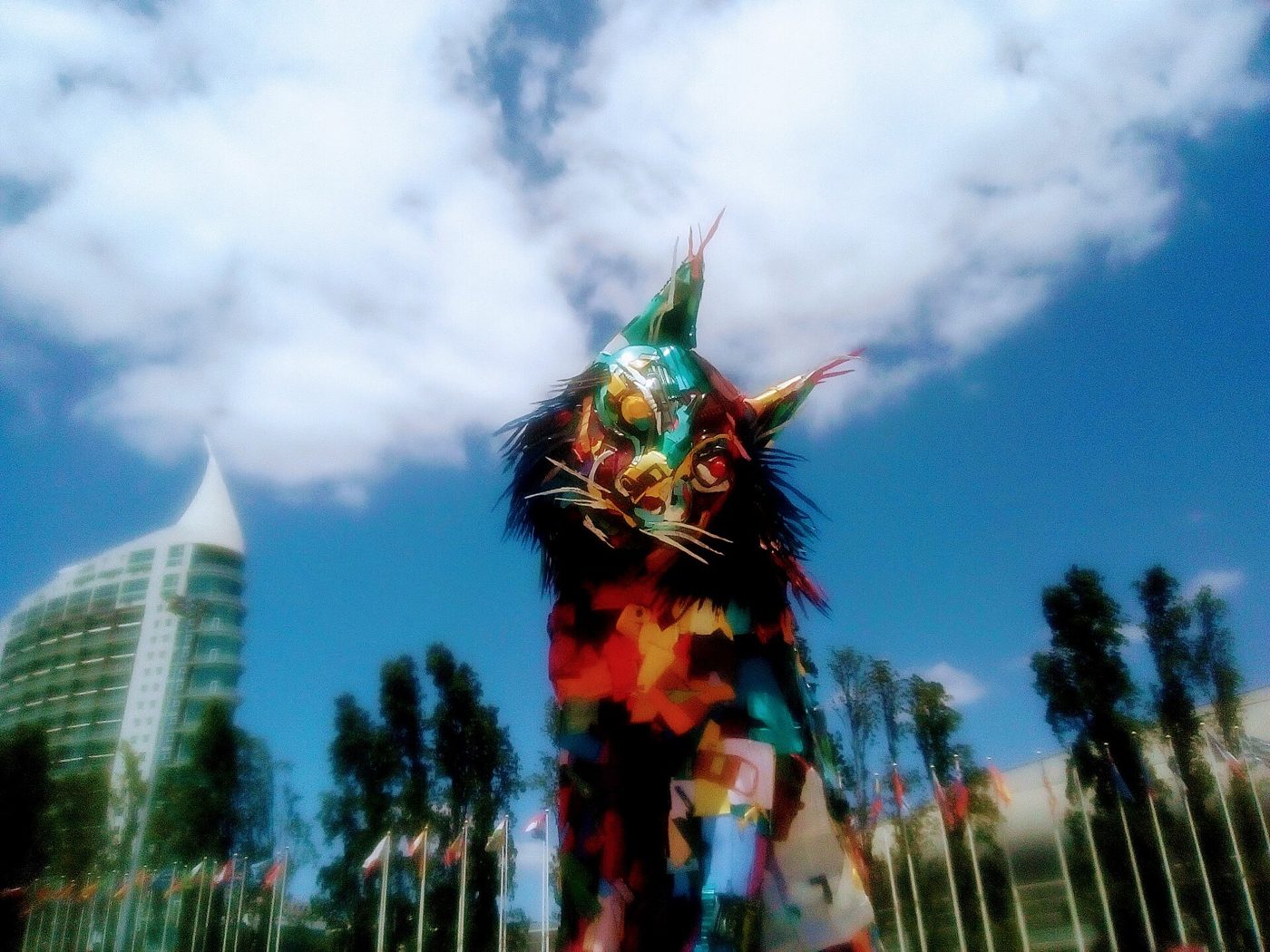 Escultura de um lince ibérico gigante, muito colorido, feito de plásticos e outros resíduos, num jardim junto a uma torre