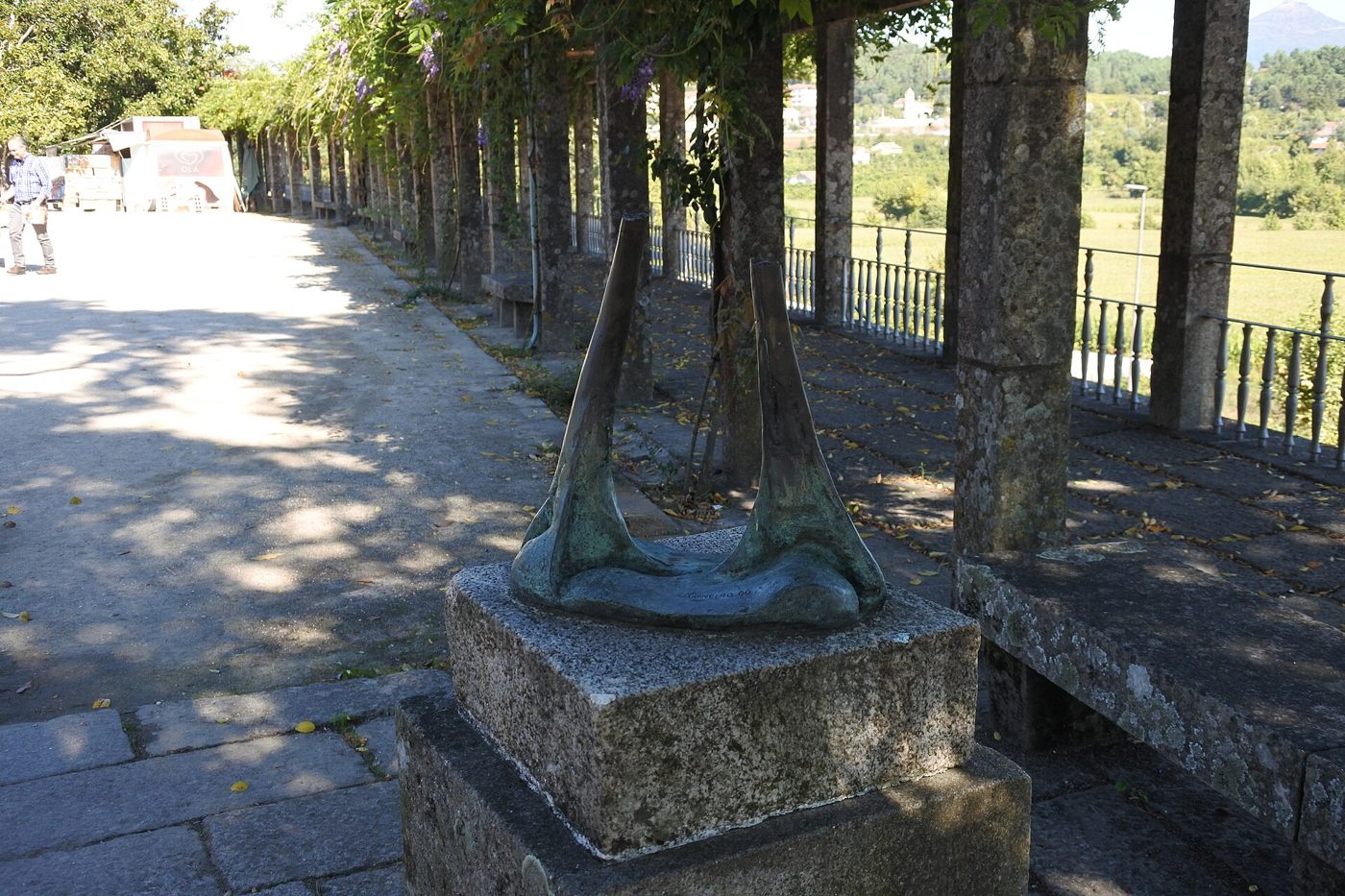 Escultura num pedestal de pedra num passeio arborizado