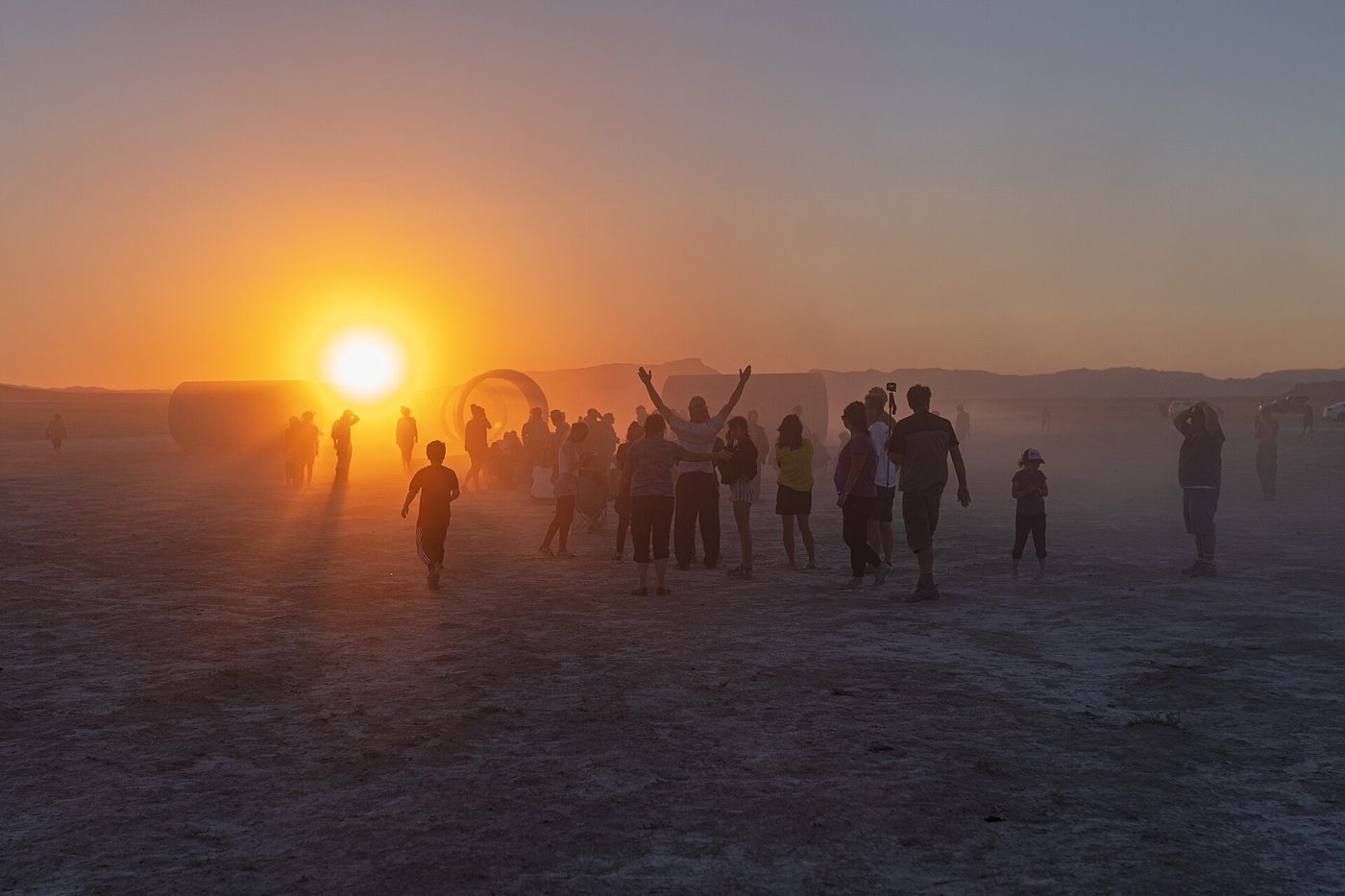 Pessoas no deserto ao pôr do sol, junto aos tubos de betão de Sun Tunnels