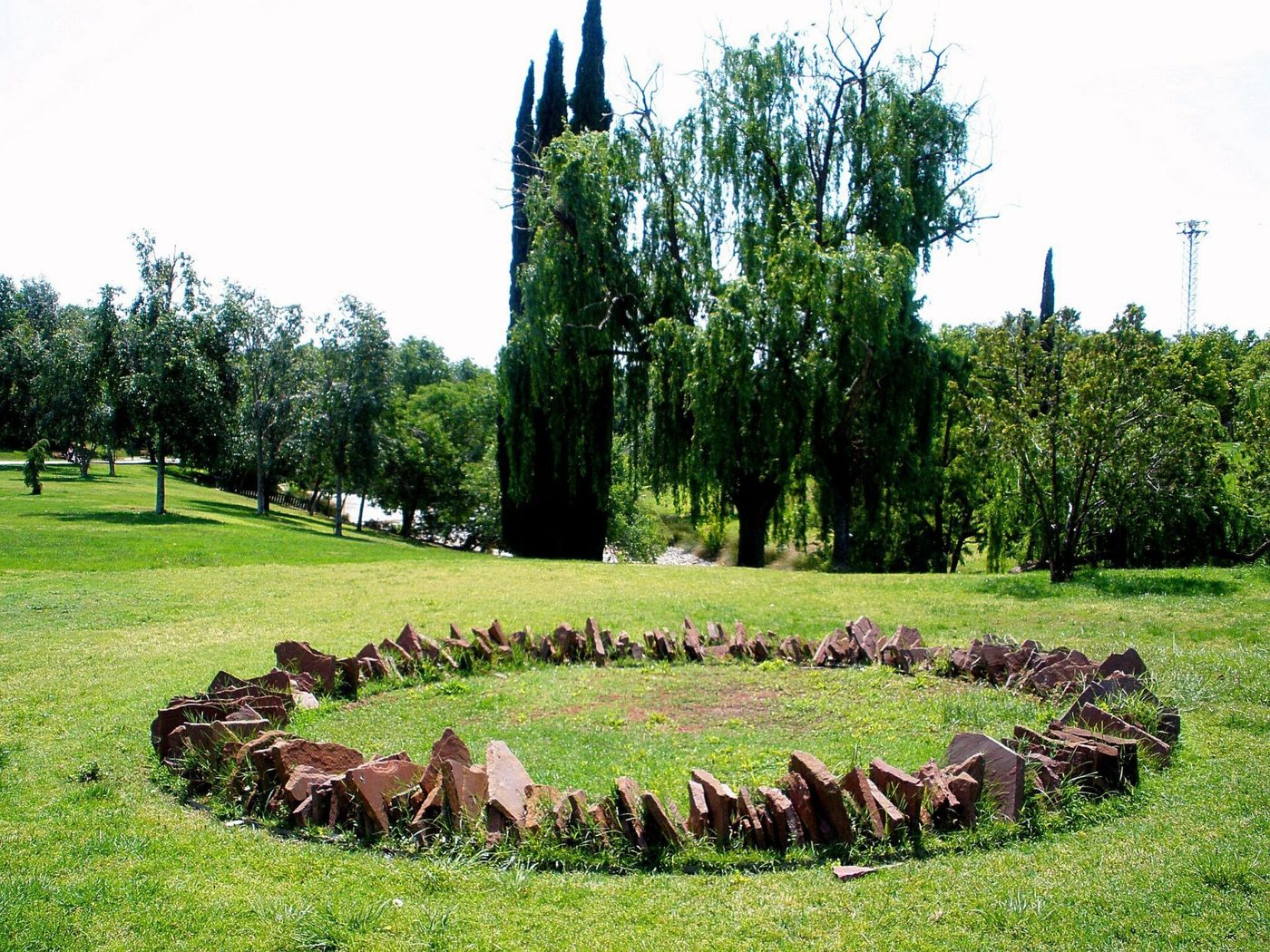 Círculo de pedras vermelhas num relvado de um parque, rodeado de árvores