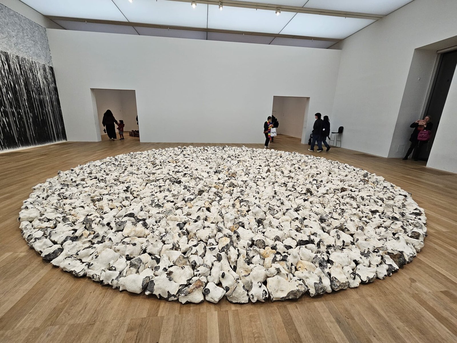 Grande círculo de pedras claras pousadas no chão de madeira de uma sala de museu
