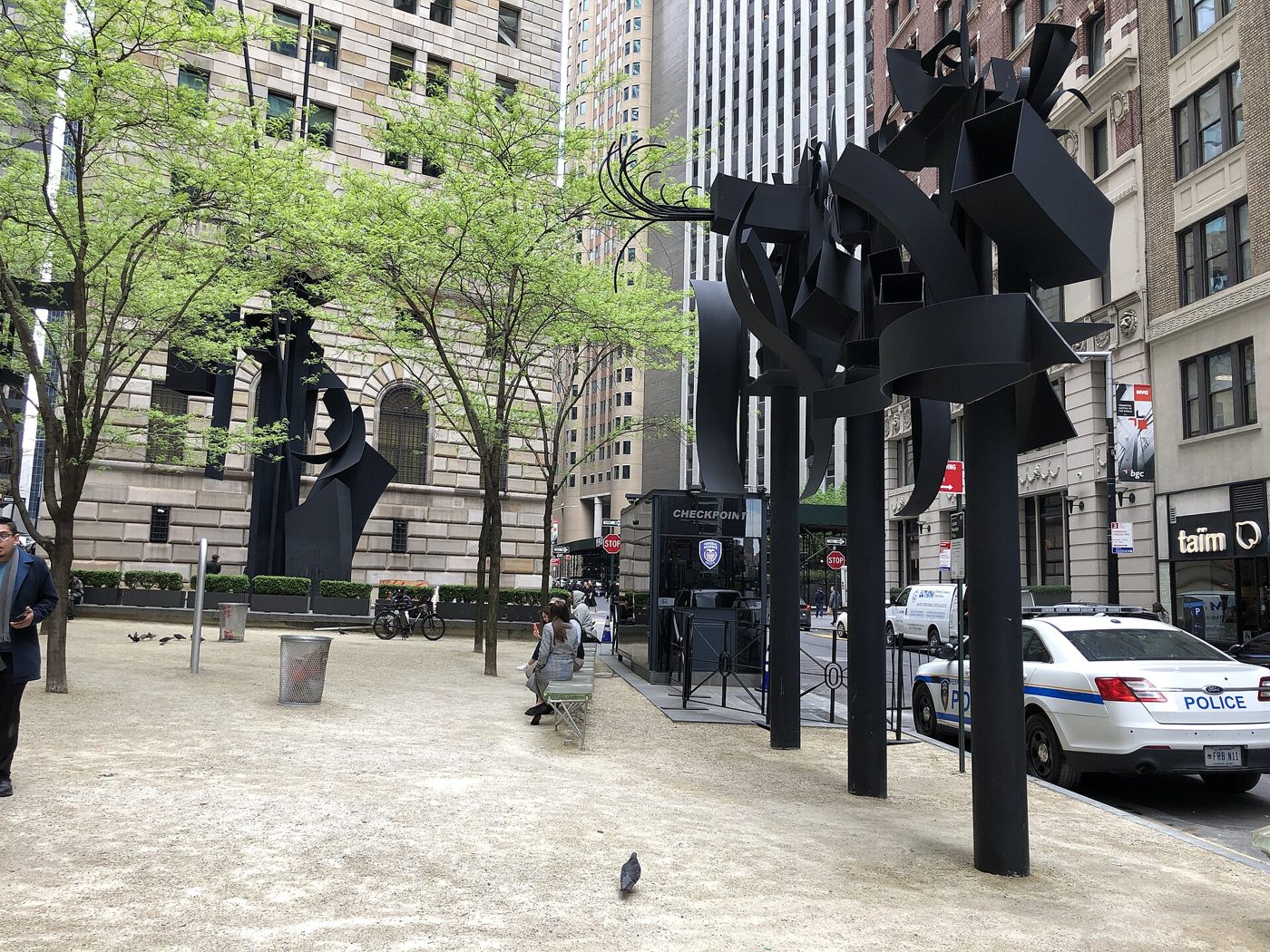 Esculturas de metal preto em postes altos numa praça entre prédios