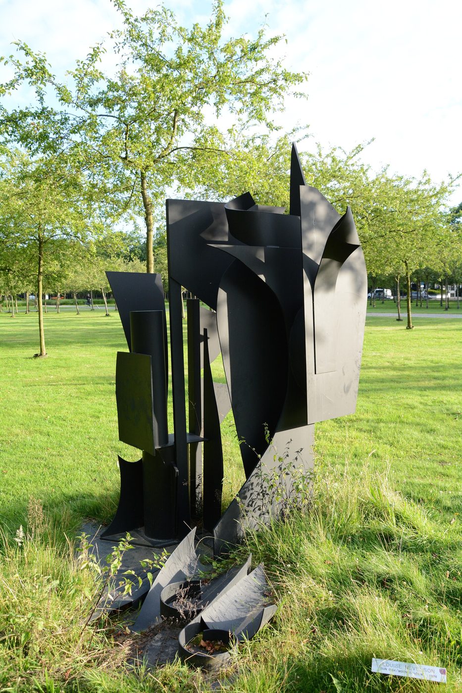 Escultura de chapas de metal preto num relvado com árvores