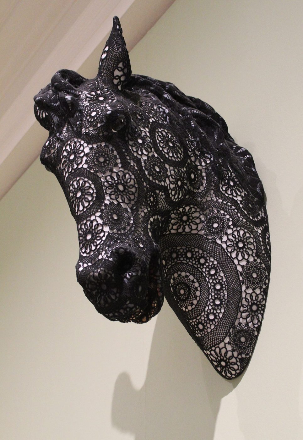 Cabeça de cavalo de cerâmica coberta por um revestimento de croché preto, pendurada numa parede