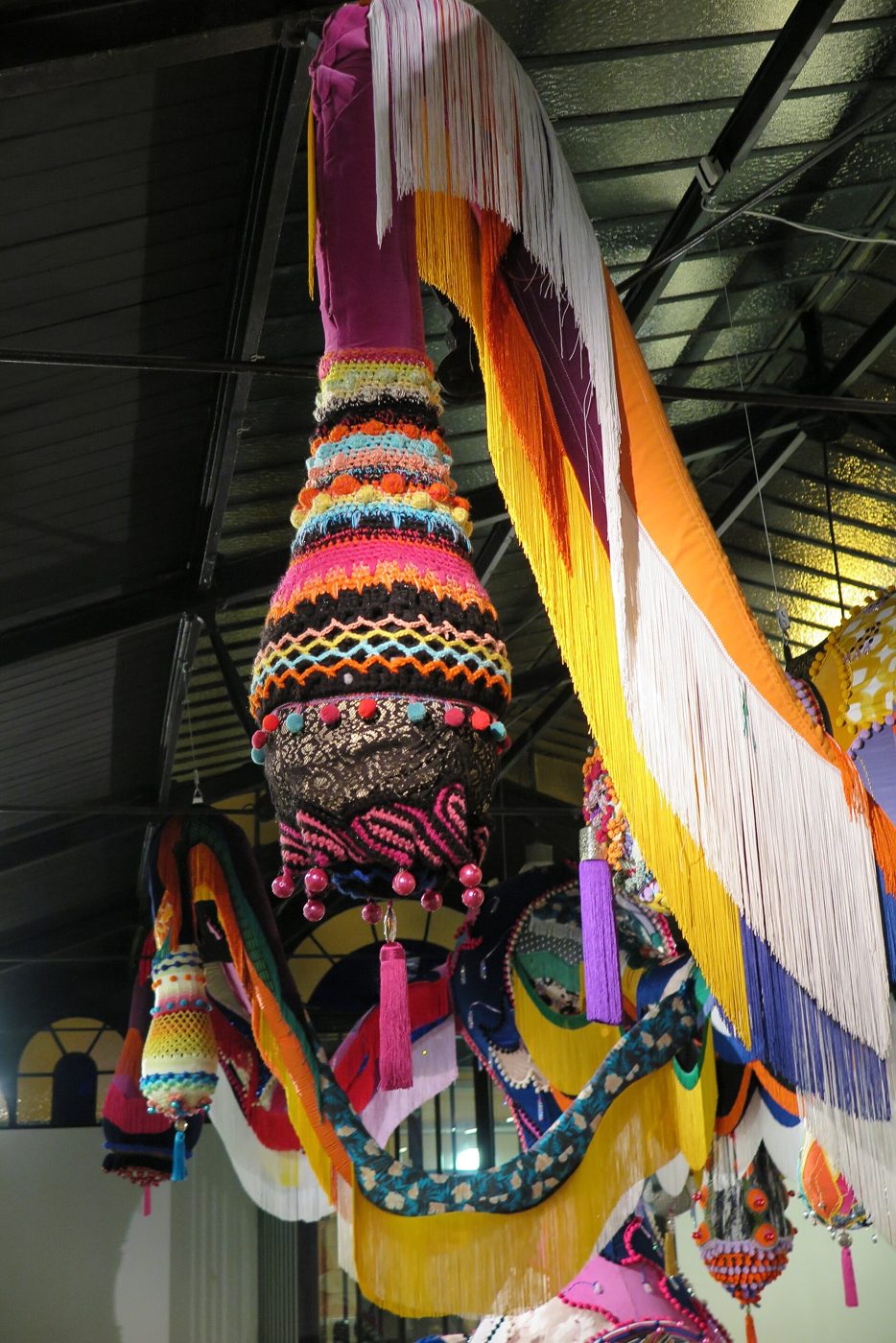 Escultura têxtil suspensa, com croché, franjas e tecidos de muitas cores